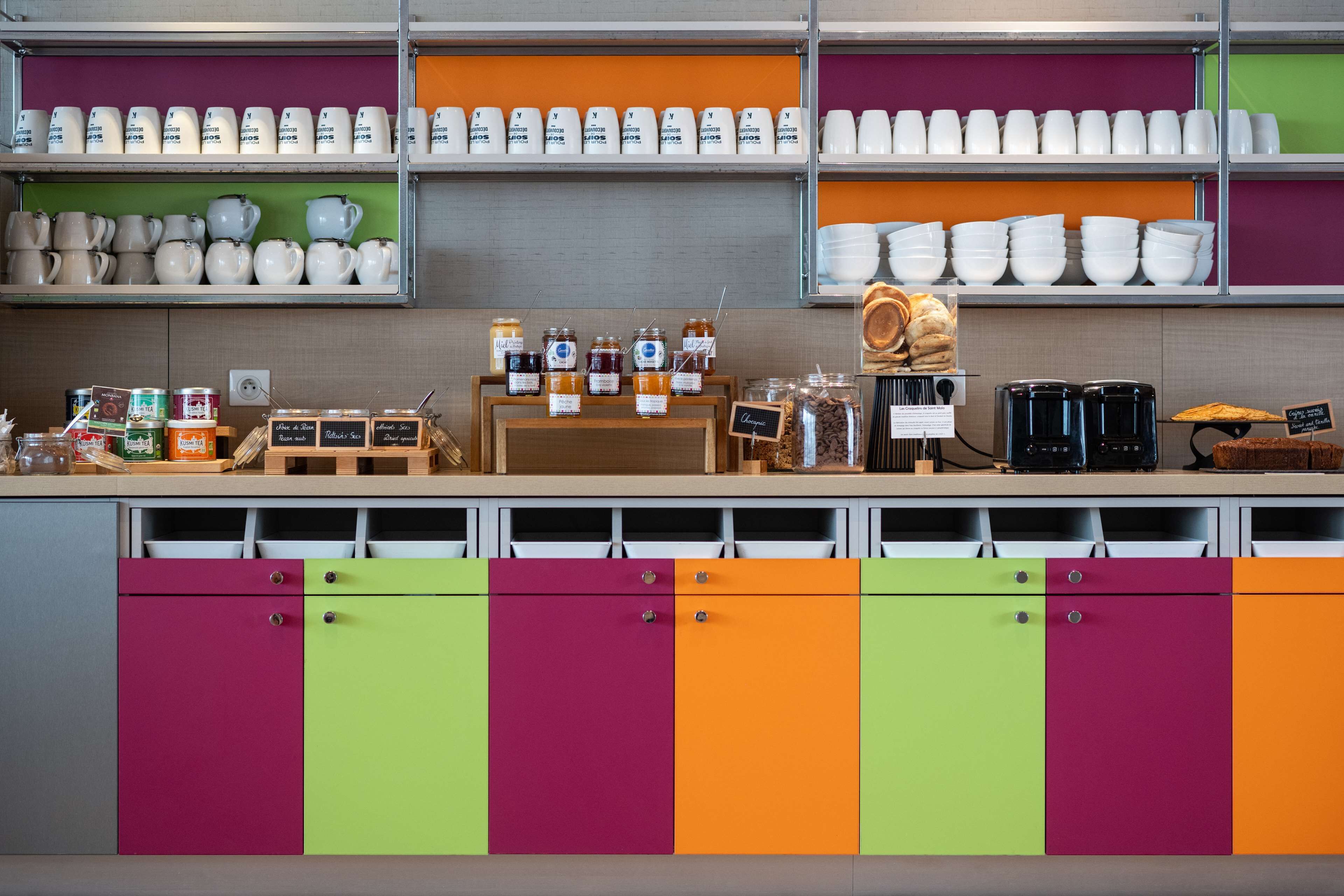 Una cocina con armarios de colores, estantes con diferentes utensilios de cocina y una estación de café.