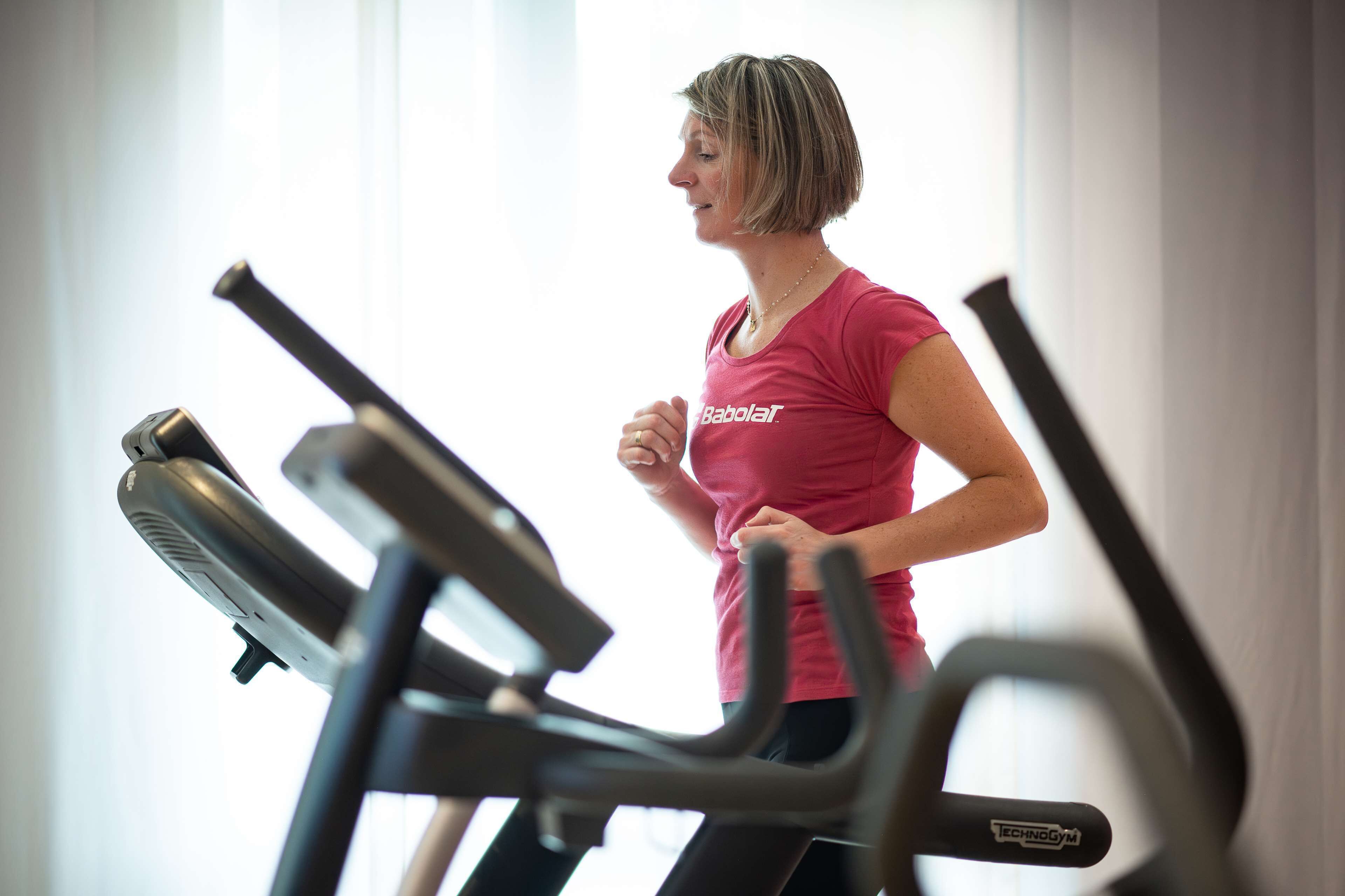 A person running on a treadmill in a gym with visible exercise equipment.