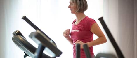 Eine Person läuft auf einem Laufband in einem Fitnessstudio mit sichtbaren Trainingsgeräten.