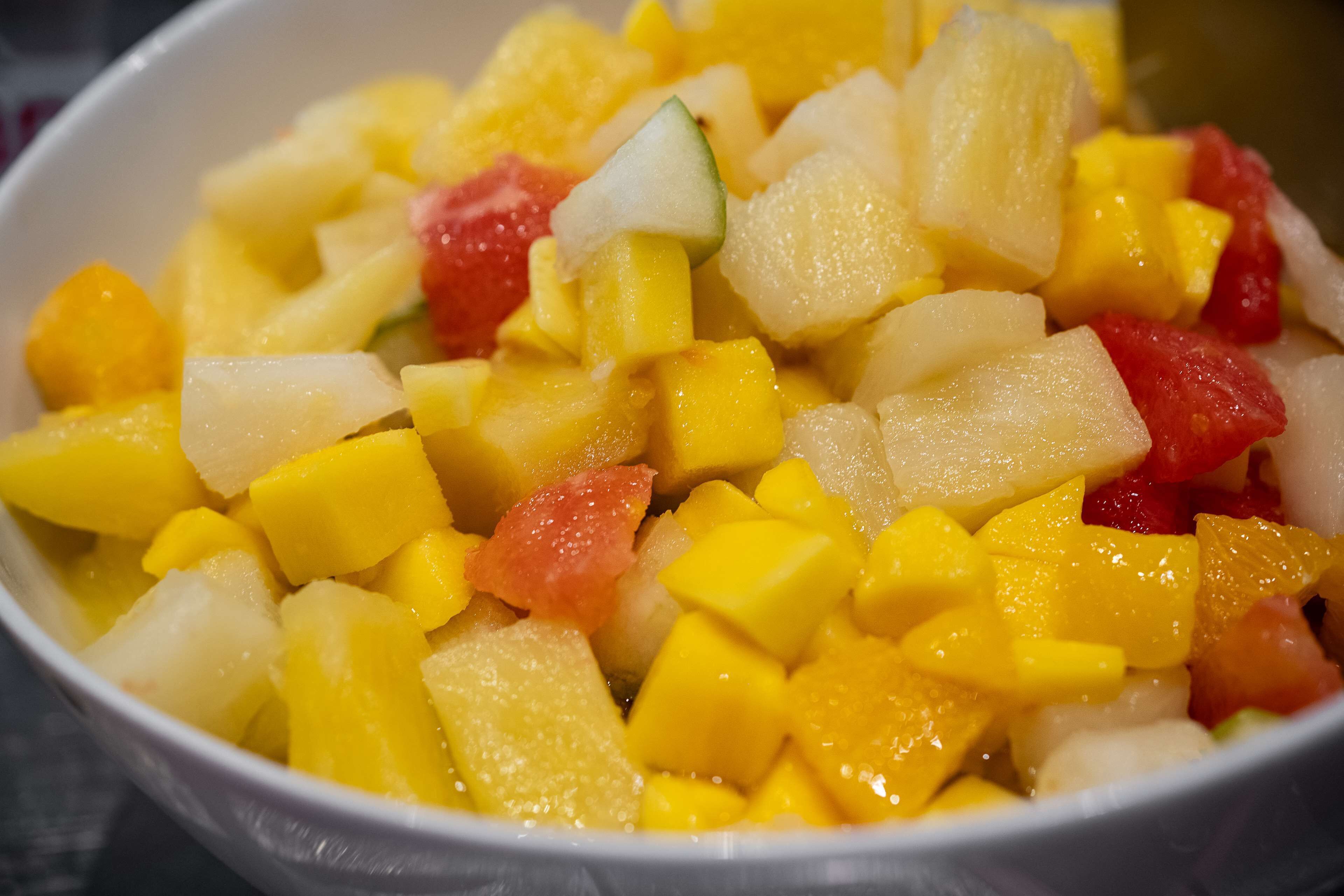 Eine Schüssel Obstsalat mit gewürfelten Früchten, darunter Mango, Ananas und möglicherweise Wassermelone.