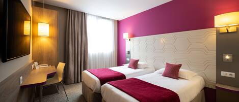 A hotel room with two beds, a desk, a chair, a TV, and a bathroom.