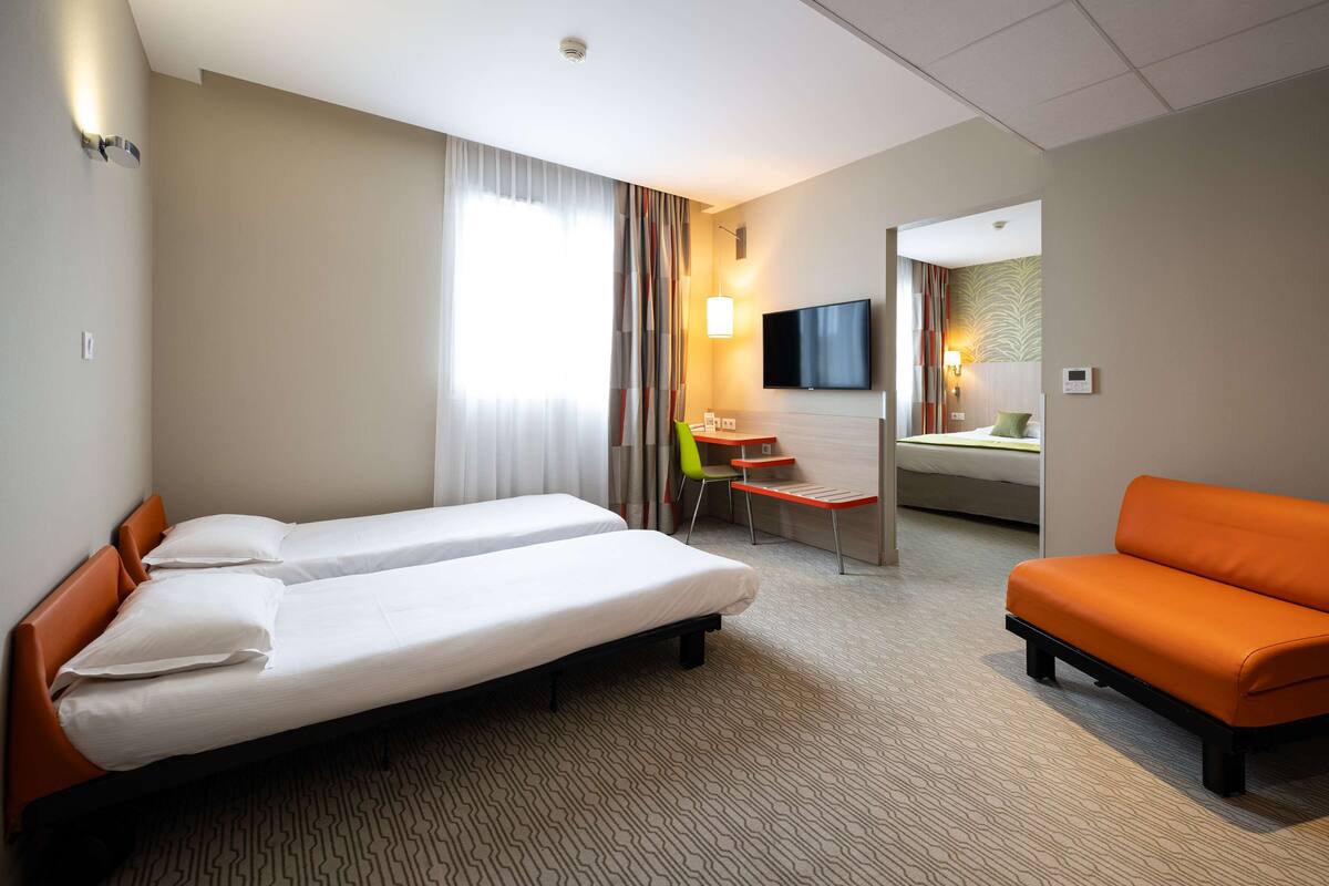 Habitación de hotel con dos camas, un escritorio, una silla, un sofá y un televisor.