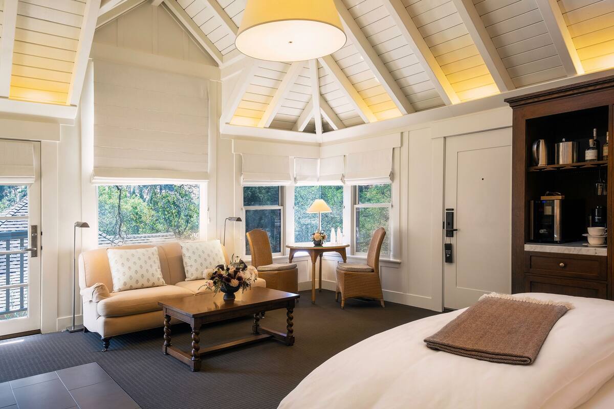 A room with a bed, a sofa, a table with flowers, and a lamp.