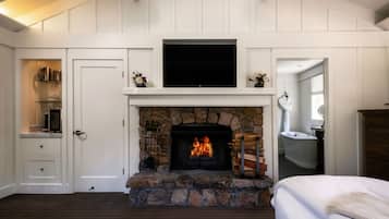 A room with a stone fireplace, a television above it, and a bed with a white blanket.