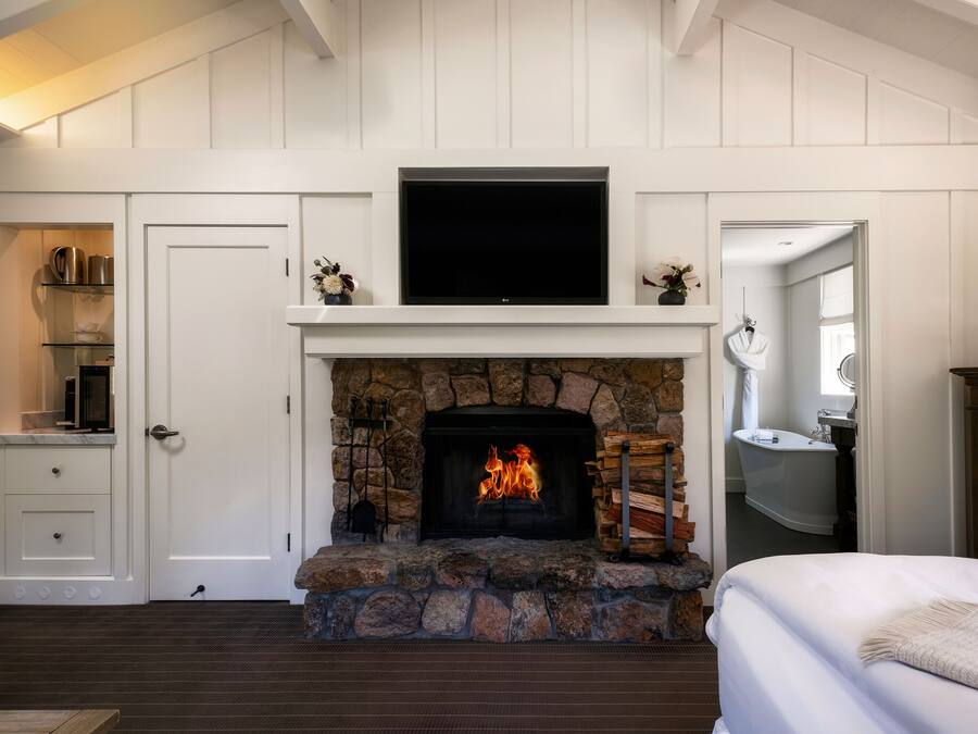 A room with a stone fireplace, a television above it, and a bed with a white blanket.