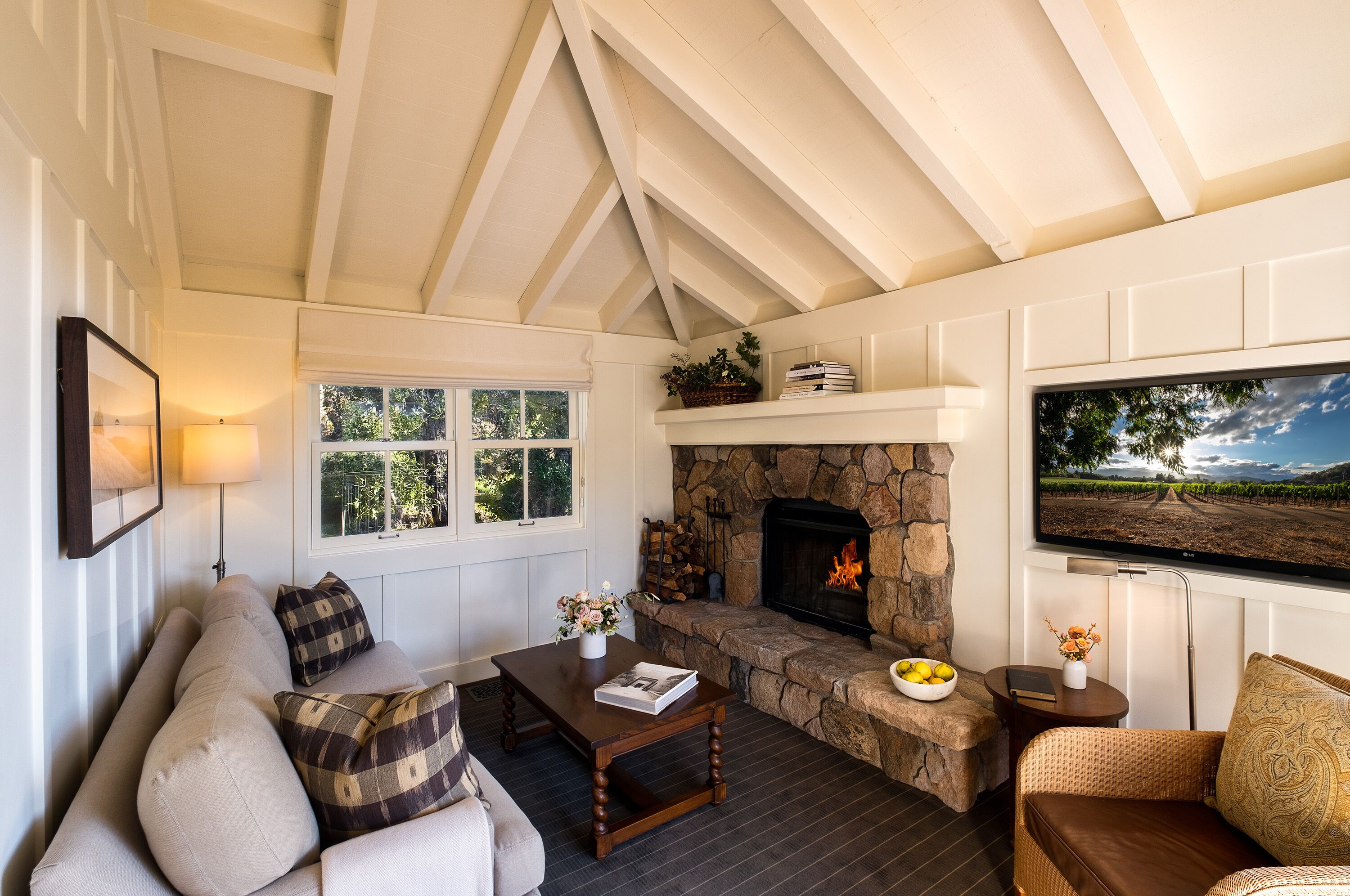 A cozy living room with a stone fireplace, a sofa, a coffee table, and a television mounted on the wall.