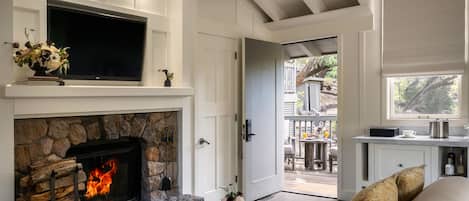 A cozy living room with a stone fireplace, a flat-screen TV mounted above it, a comfortable sofa, and a view into the outdoor patio area.