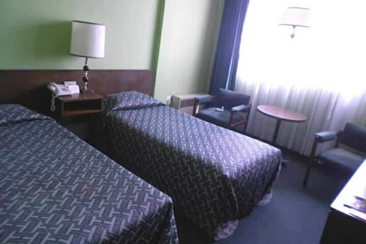 A hotel room with two beds, a desk with a lamp, a chair, a small table, and a window with curtains.