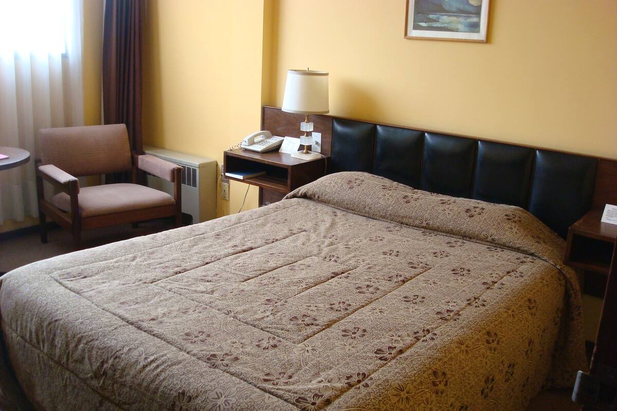 A hotel room with a large bed, a chair, a desk with a lamp, and a painting on the wall.