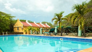 A swimming pool with clear blue water, surrounded by a wooden deck and a small building with a red roof. - Landhuis Daniel Hotel (Daniel)