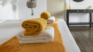 A neatly made bed with rolled towels, a hanging plant, a mirror, and a dark wooden desk in a room with white walls and a sloped ceiling. - Landhuis Daniel Hotel (Daniel)
