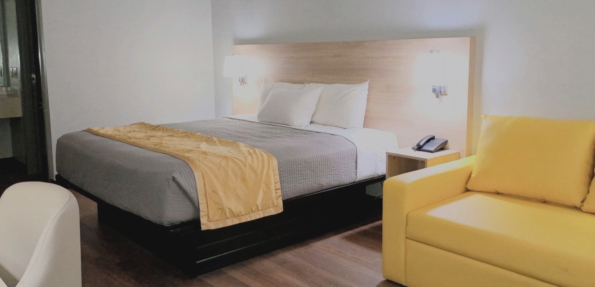 A hotel room with a bed, bedside table, and a yellow armchair.