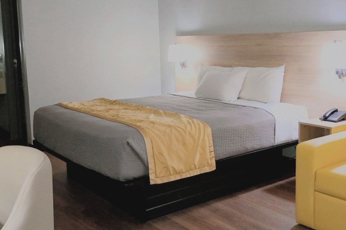 A hotel room with a bed, bedside table, and a yellow armchair.