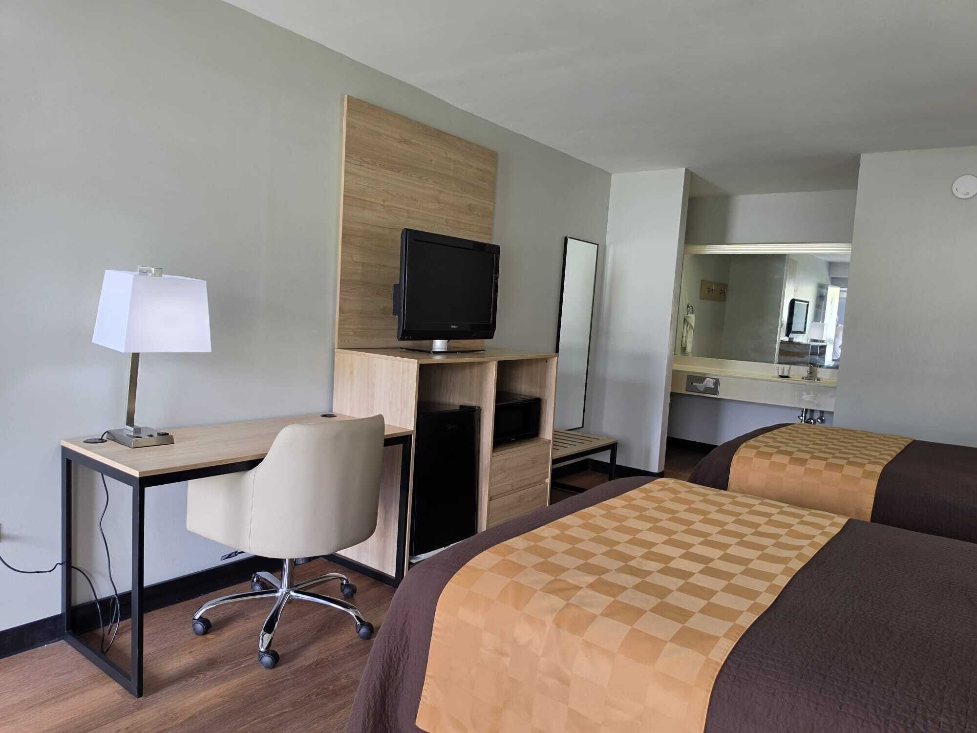 A hotel room with a desk, chair, television, and two beds.