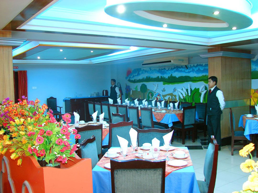 Un restaurant amb diverses taules preparades per dinar, un cambrer atent als comensals i un mural a la paret.