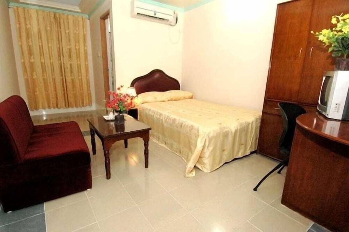 A small, neatly arranged room with a bed, a desk, a chair, a TV, and a wardrobe.