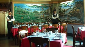 Un restaurante con mesas dispuestas para comer, un mural en la pared y personal de servicio.