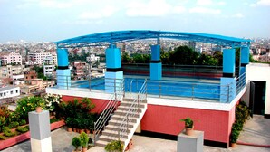 Una terraza en la azotea con un toldo azul, escalones de acceso y plantas en macetas.