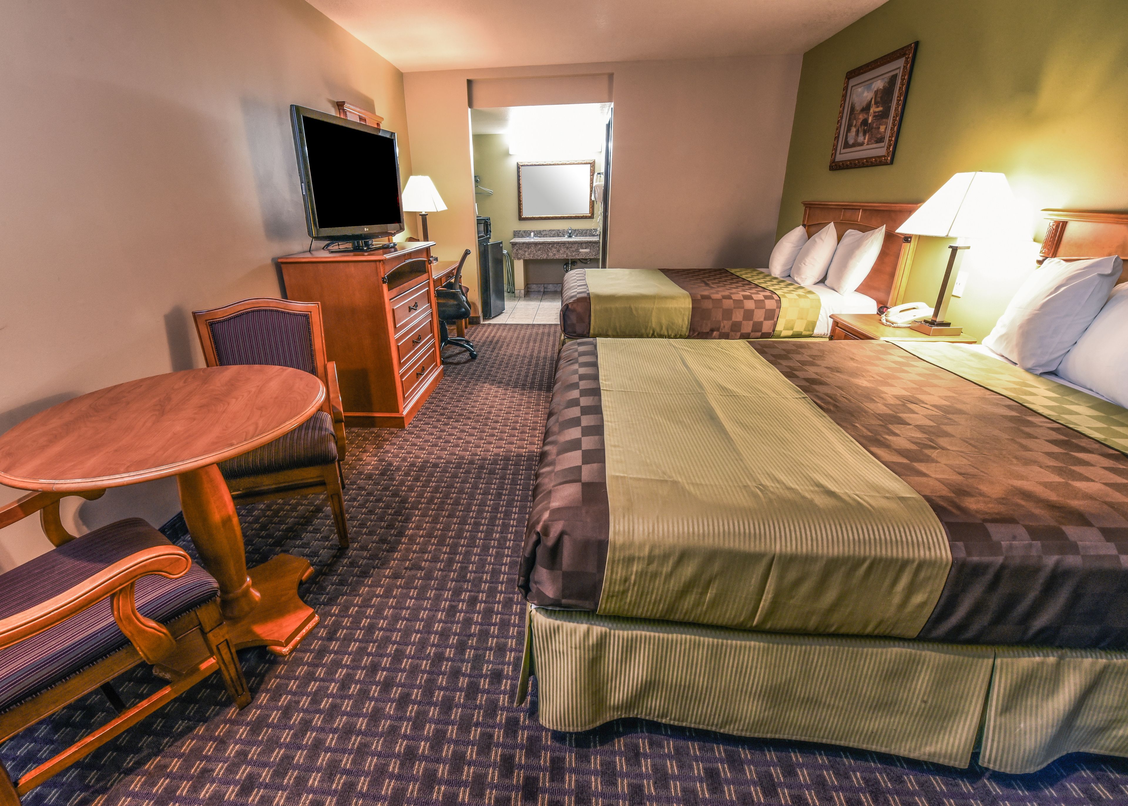 Ein Hotelzimmer mit zwei Betten, einem Schreibtisch mit Stuhl, einem Fernseher, einer Schreibtischlampe und einem sichtbaren Badezimmer hinter einer offenen Tür.