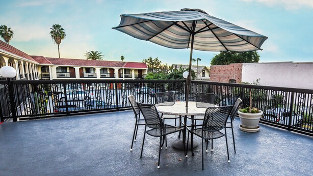 Een balkon met een ronde tafel, vier stoelen, een grote parasol en een bloempot.