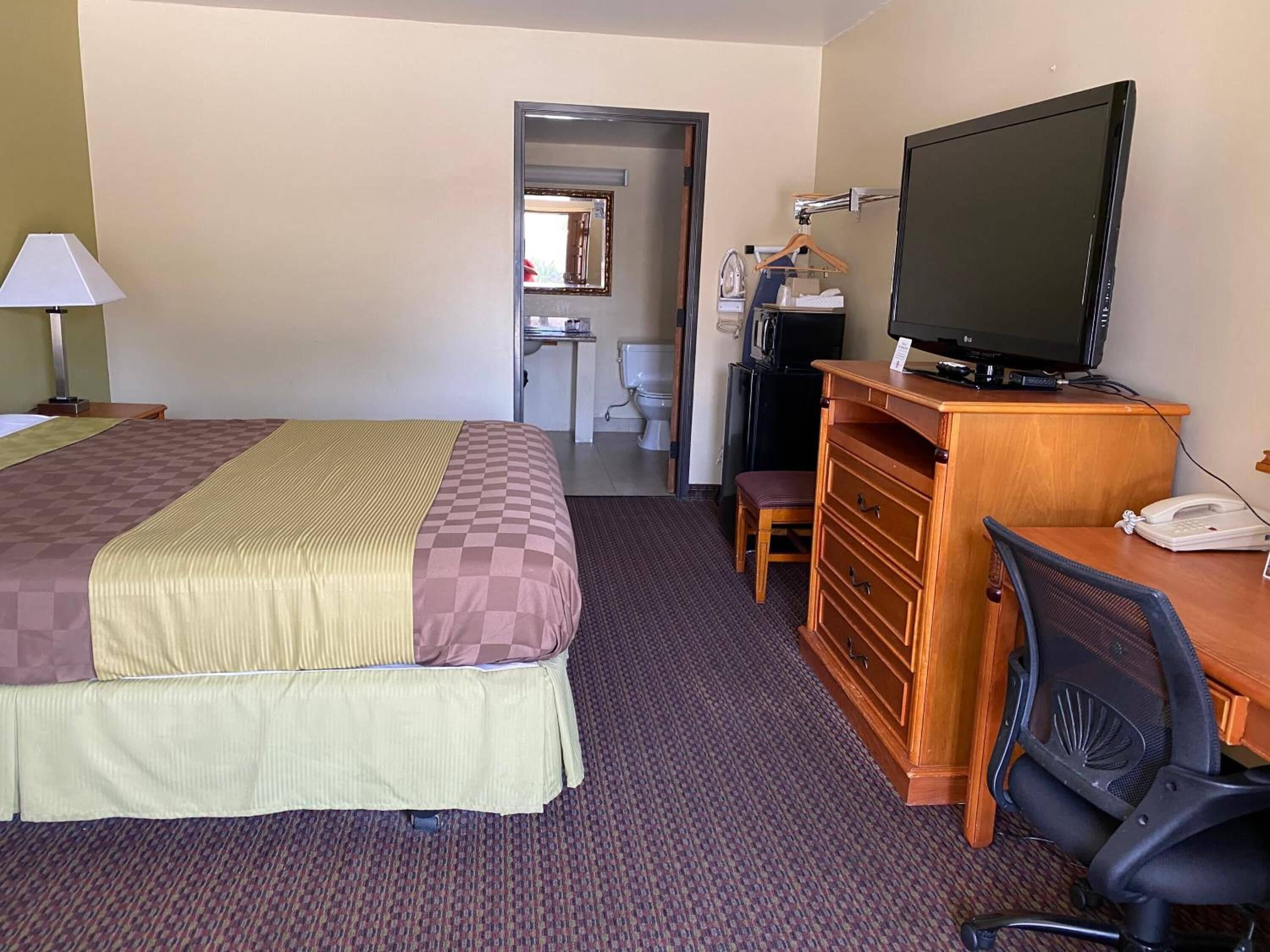 Ett hotellrum med en säng, ett skrivbord med en dator, en tv, en stol och en telefon.