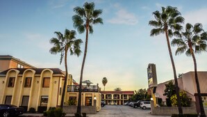 Een hotel met een centrale binnentuin, palmbomen en een parkeerplaats.