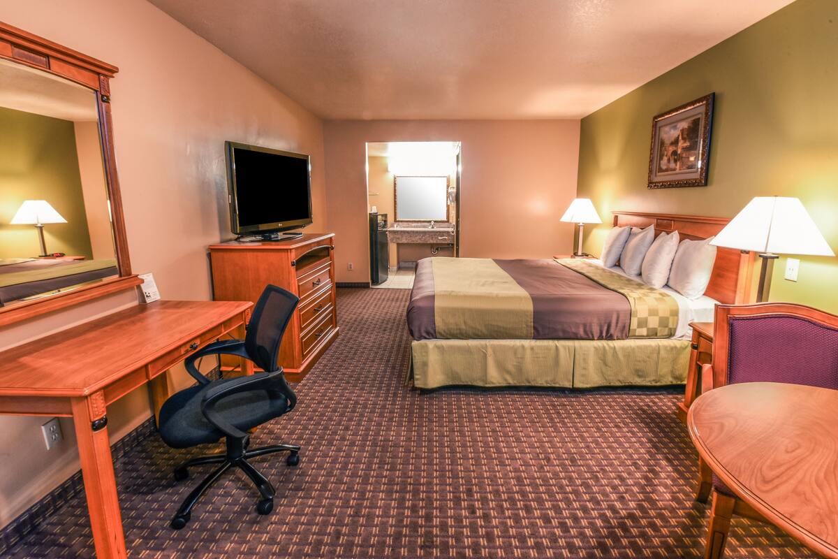 A hotel room with a bed, desk, chair, television, and a bathroom visible through an open door.
