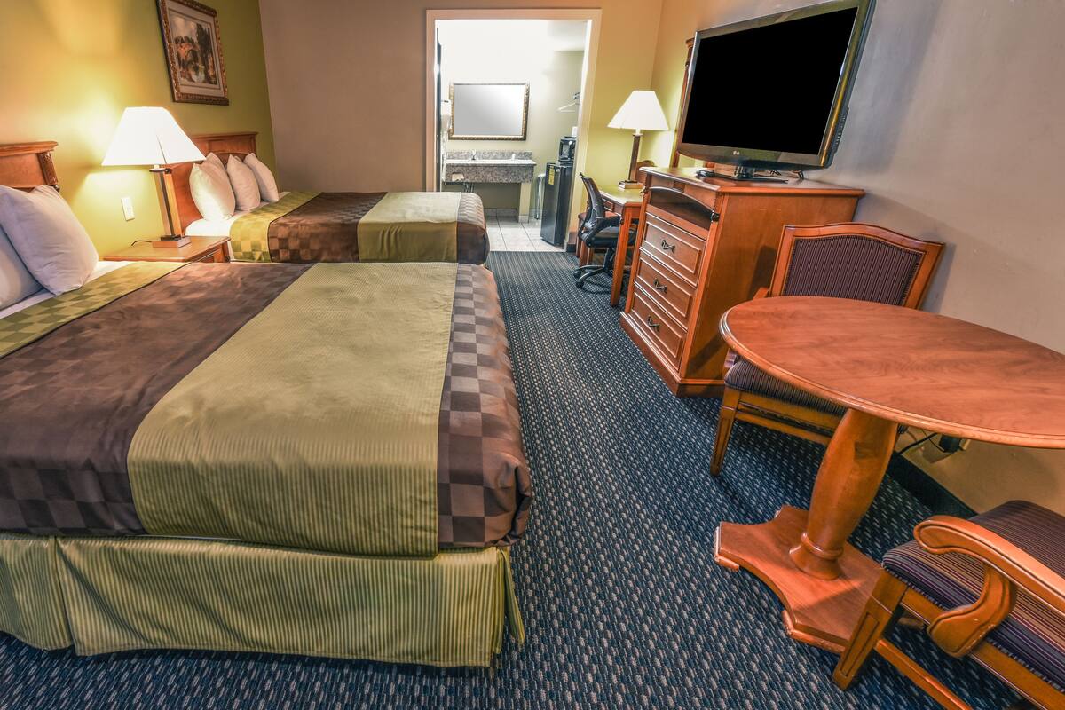A hotel room with two beds, a desk, a chair, a TV, and a bathroom visible through an open door.