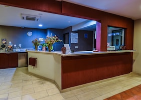 A hotel reception area with a counter, a clock, and a sign indicating a maximum occupancy of 20 persons.