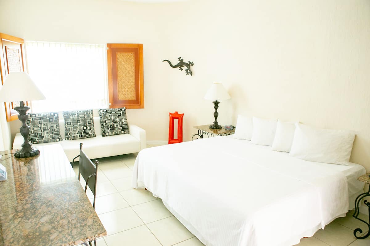 Habitación de hotel con una cama grande, un sofá, una mesa de comedor y una mesita de noche con lámpara.