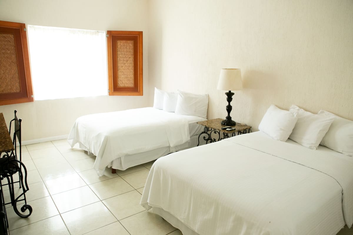 Una habitación de hotel con dos camas, una mesita con lámpara y una silla.