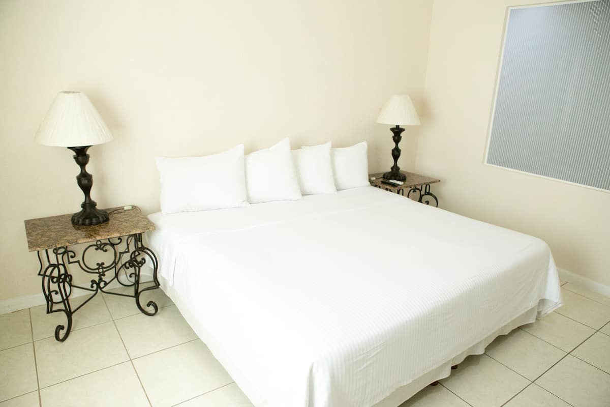 Una cama bien hecha con sábanas blancas en una habitación con paredes color crema y suelo de baldosas.