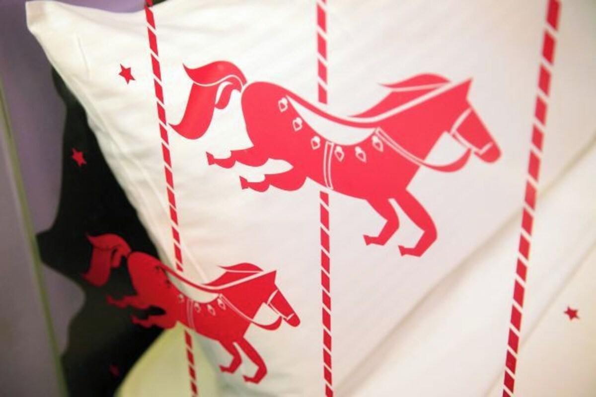 Un coussin orné de motifs représentant des chevaux rouges et doté d’une bordure rayée.