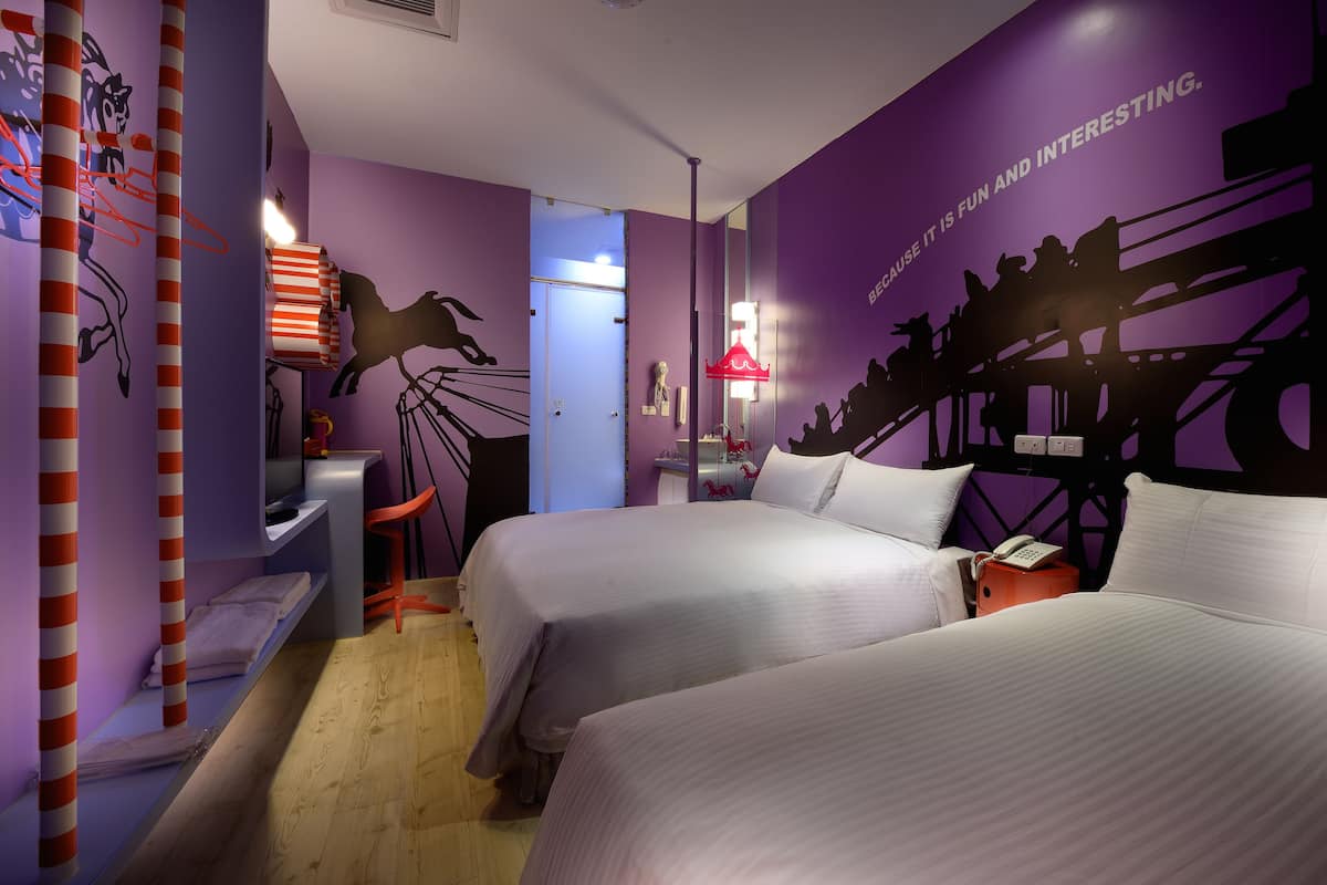 A hotel room with two beds, a desk, a chair, and a wall mural.