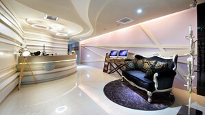 A modern reception area with a curved desk, two monitors, a plush sofa, and a decorative lamp. - NL Concept Hotel (Kaohsiung)