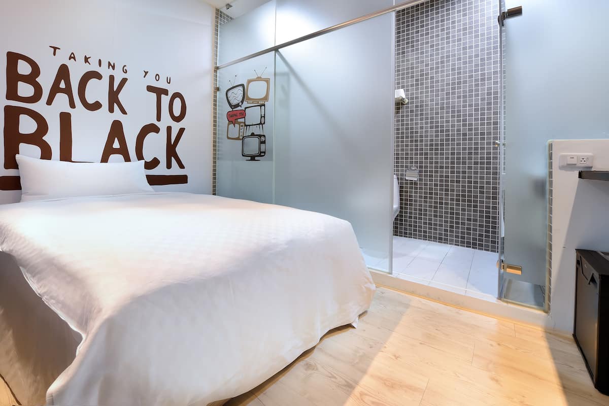A bedroom with a bed, a wall with a 'Taking you Back to Black' sign, and a shower area.