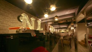 A modern interior with a large illuminated 'N' sign, wooden flooring, and a mix of seating areas including a red chair. - NL Concept Hotel (Kaohsiung)