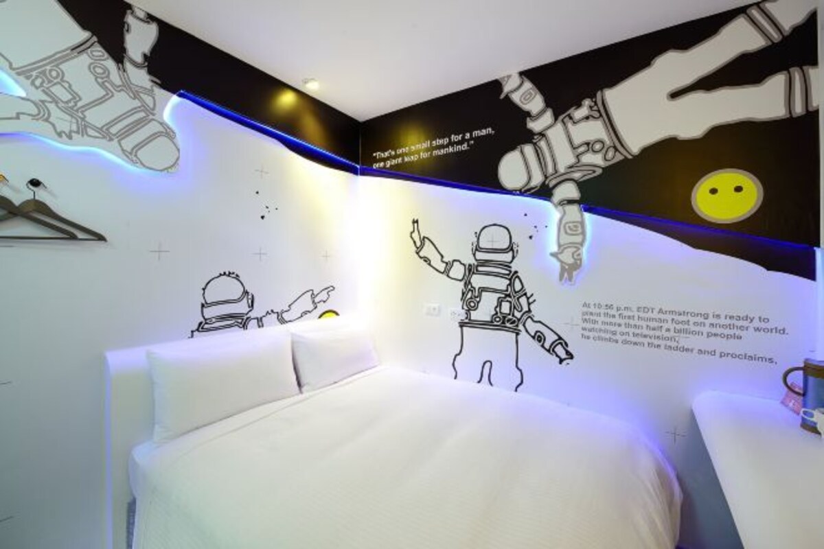 Une chambre avec un lit, un mur orné de dessins d’astronautes et un texte sur une mission spatiale.