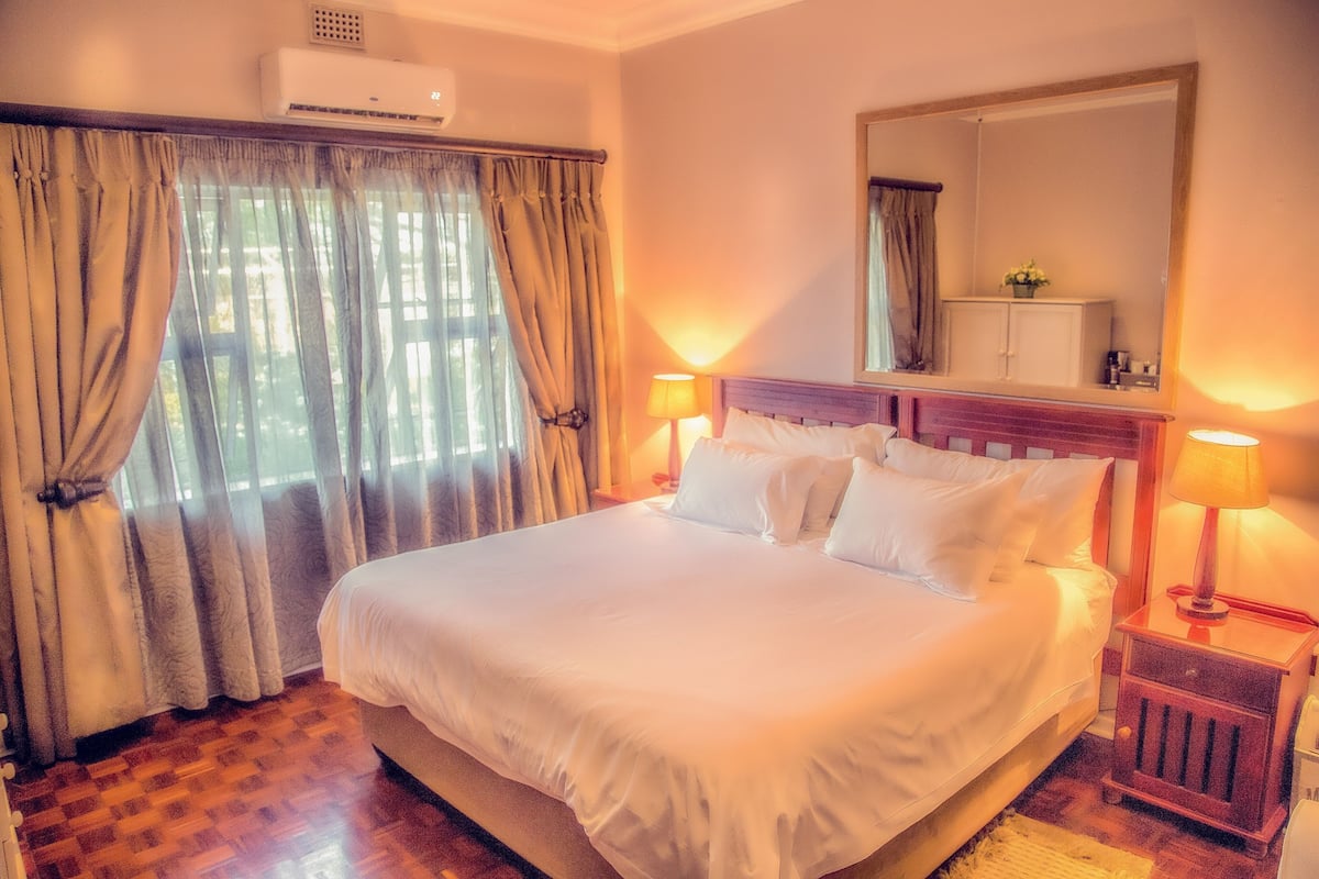 A neatly made bed with white linens, a wooden headboard, and two bedside lamps.