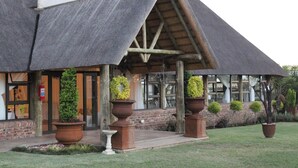 Un bâtiment doté d’un toit en pente, de grandes fenêtres et de plantes en pot devant l’entrée.