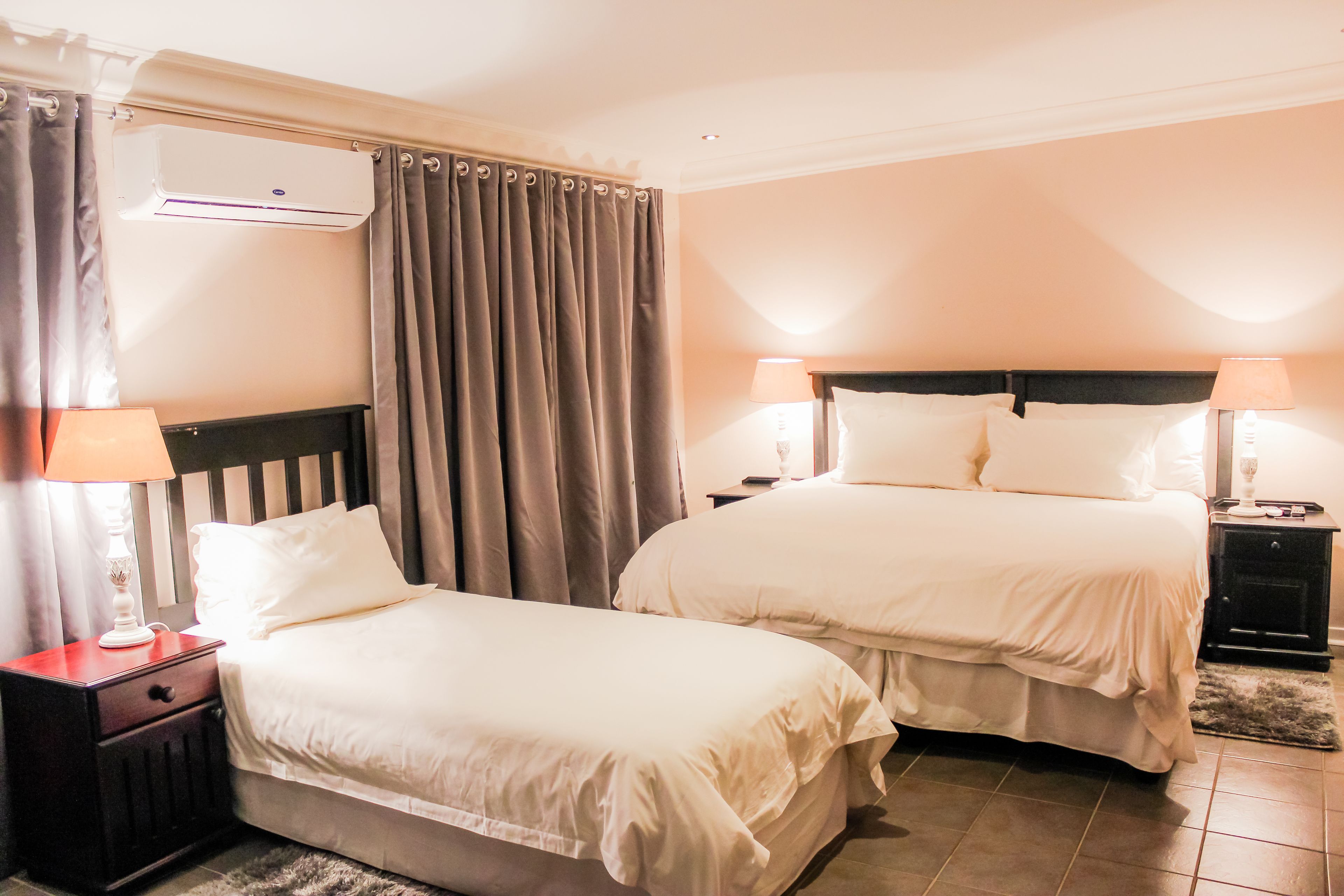 Une chambre d’hôtel avec deux lits, une table de chevet avec une lampe, un appareil de climatisation et un rideau.