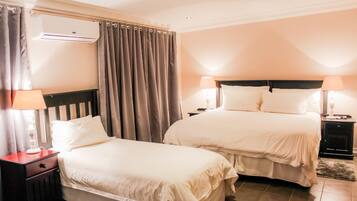 Une chambre d’hôtel avec deux lits, une table de chevet avec une lampe, un appareil de climatisation et un rideau.