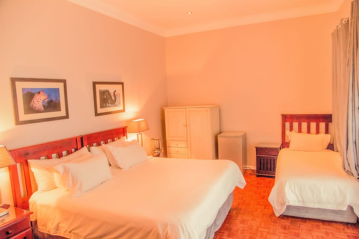 A hotel room with two beds, a wardrobe, a nightstand, and a lamp.