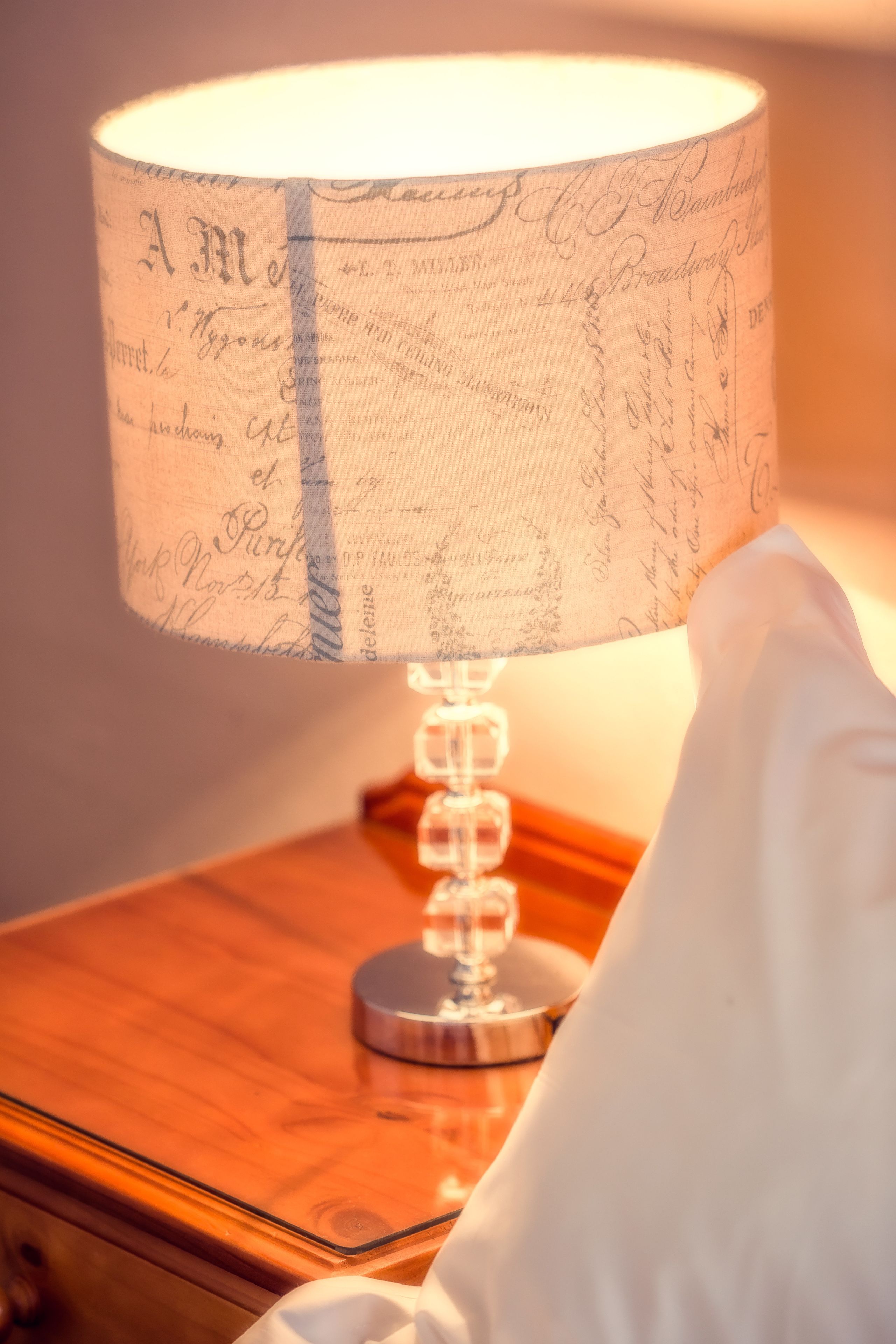 Eine Lampe mit einem gemusterten Lampenschirm auf einem Nachttisch aus Holz.