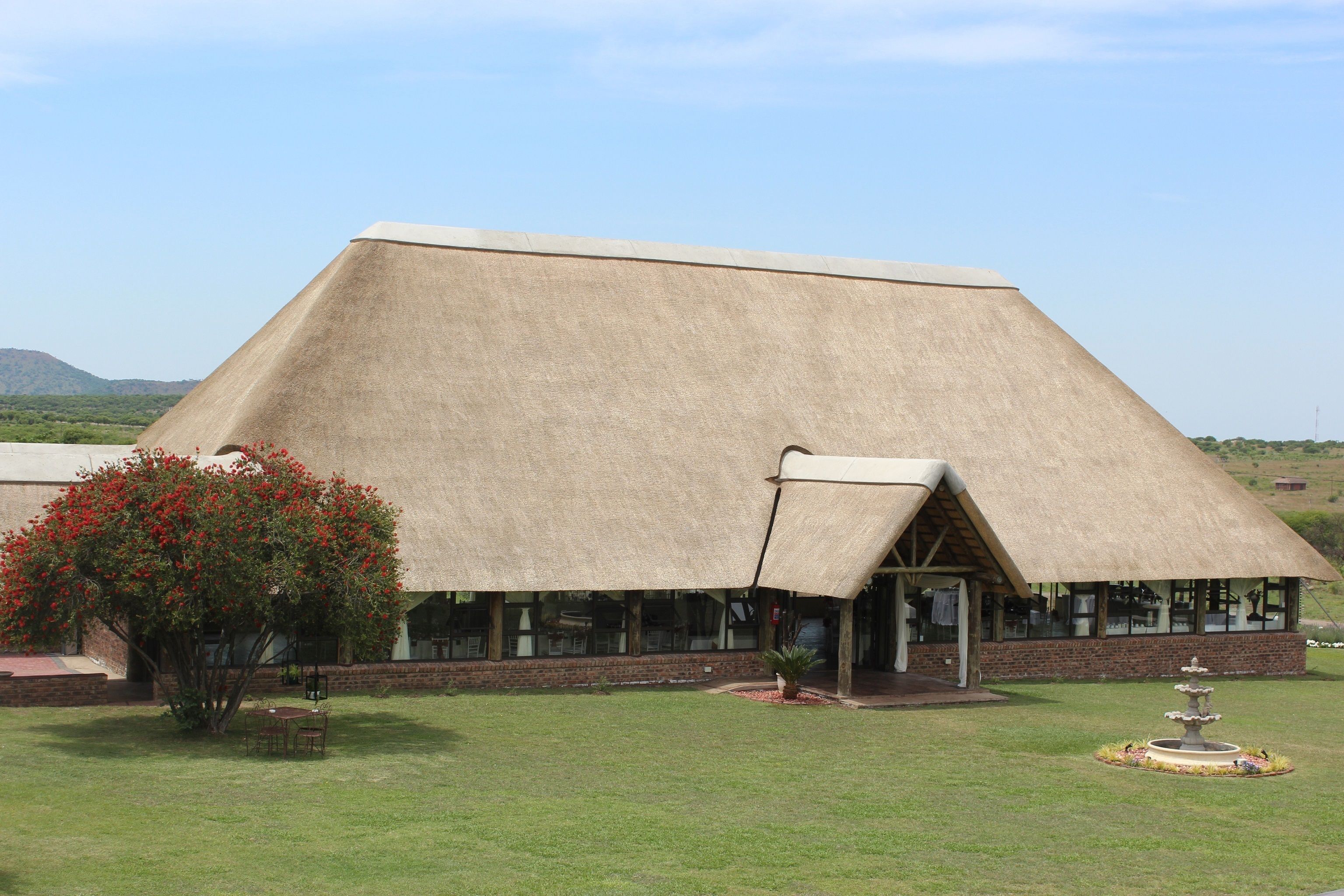 A building with a large thatched roof, a brick lower section, and a small garden area with a fountain.
