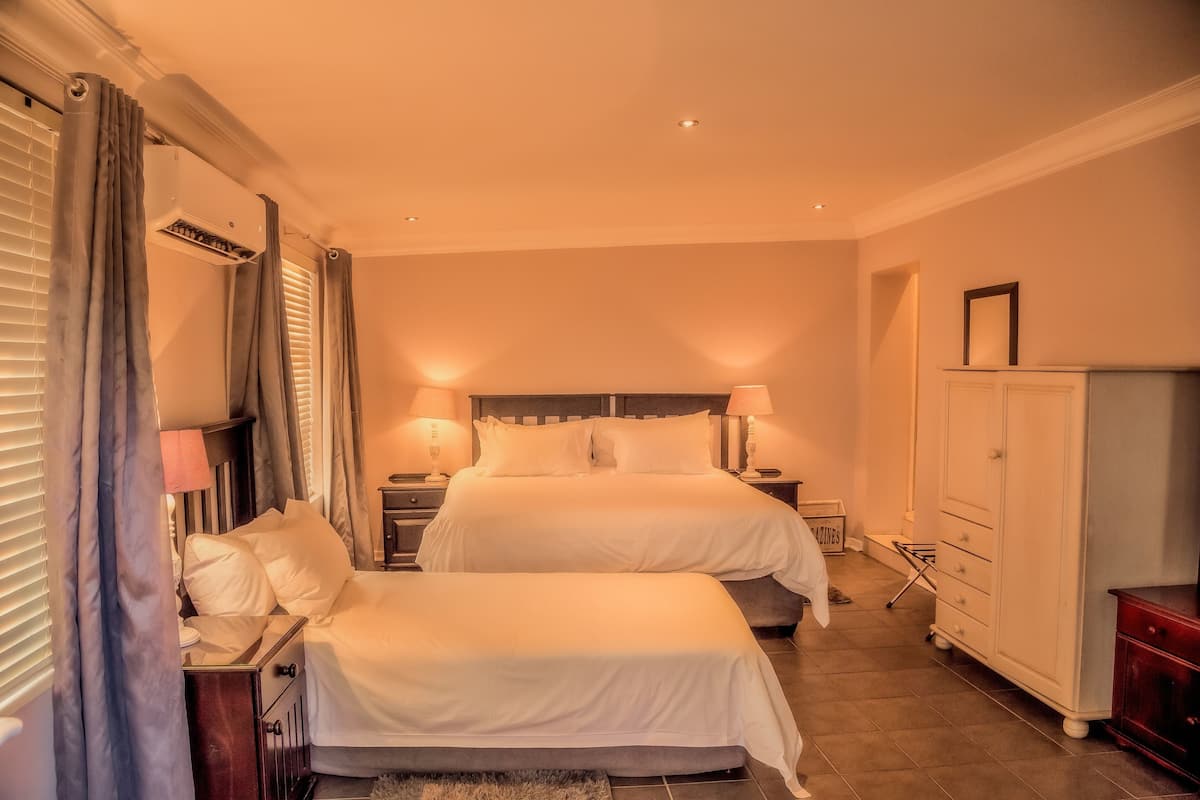 A hotel room with two beds, a wardrobe, a nightstand, and a lamp.