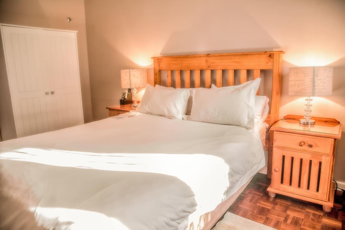 A neatly made bed with a wooden headboard, a nightstand with a lamp, and a wall-mounted light fixture.