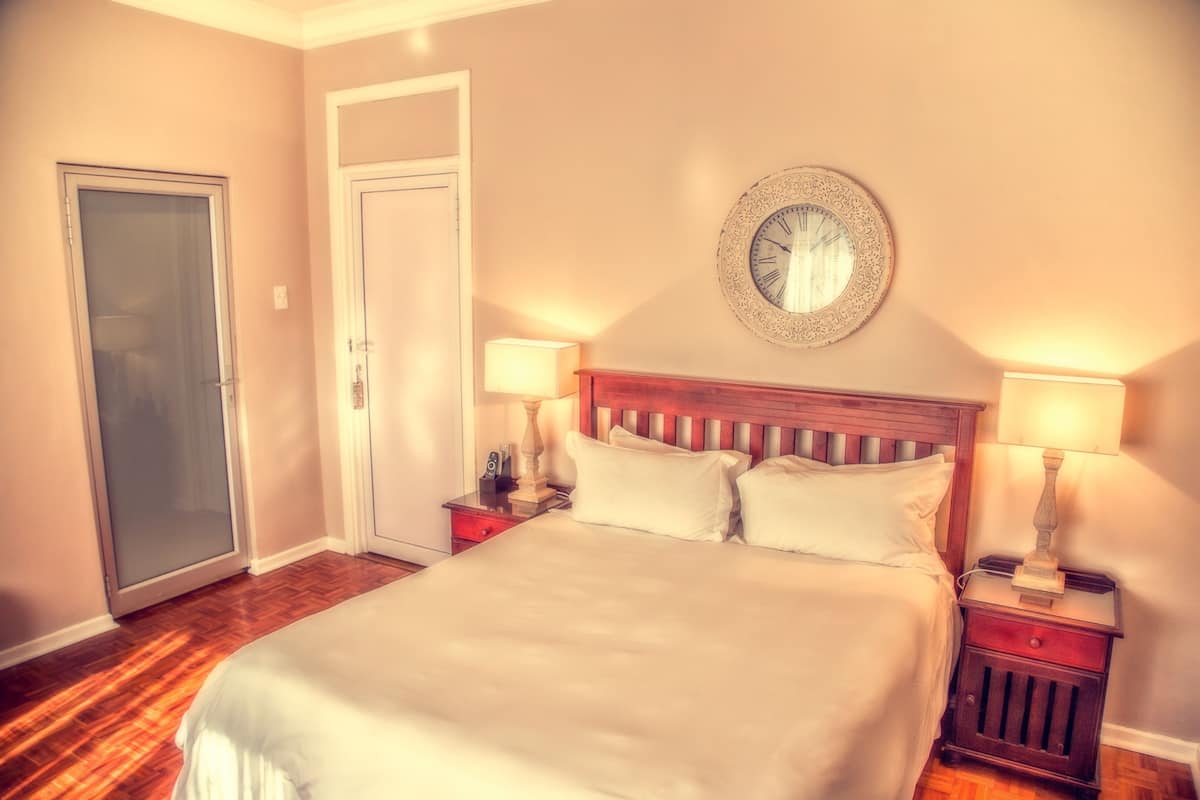 A bedroom with a bed, two bedside tables, a wall clock, and a door.