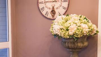 A room with a clock, a vase of flowers, and a chest of drawers.