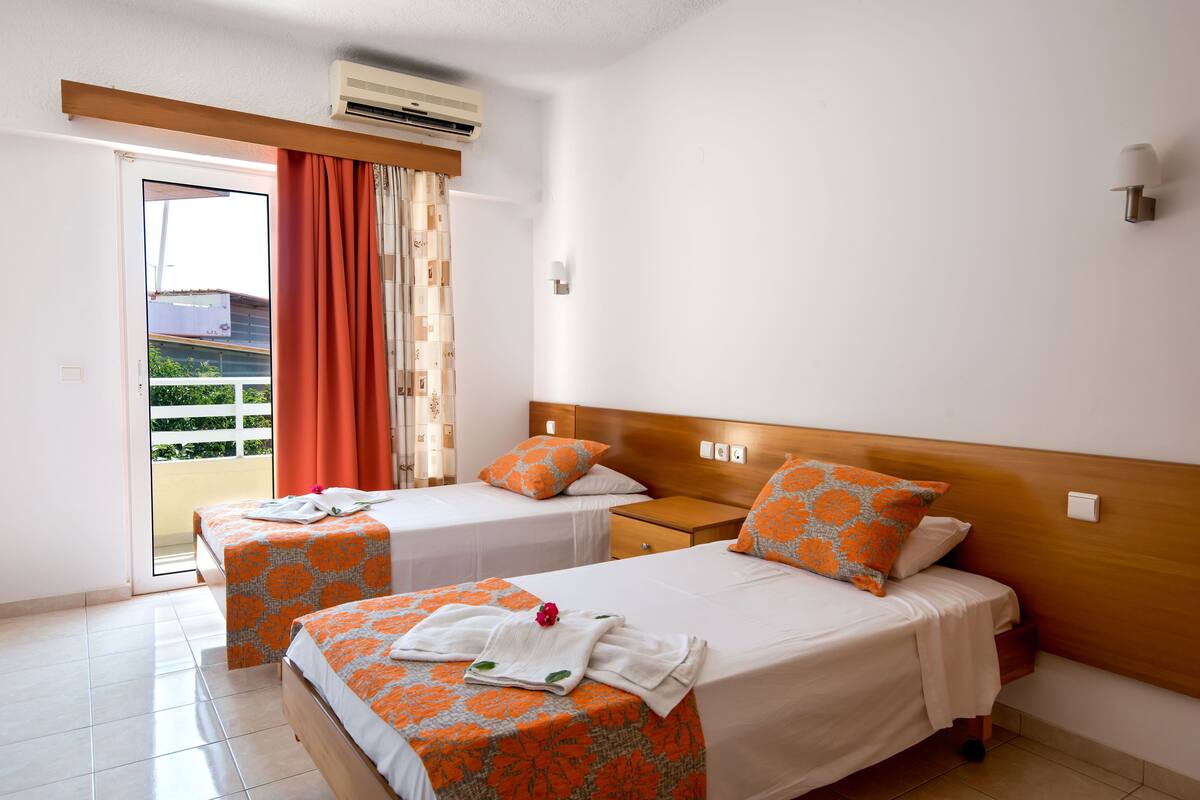 Ein Hotelzimmer mit zwei Betten, einem Balkon, einer Klimaanlage und einem Holzkopfende.